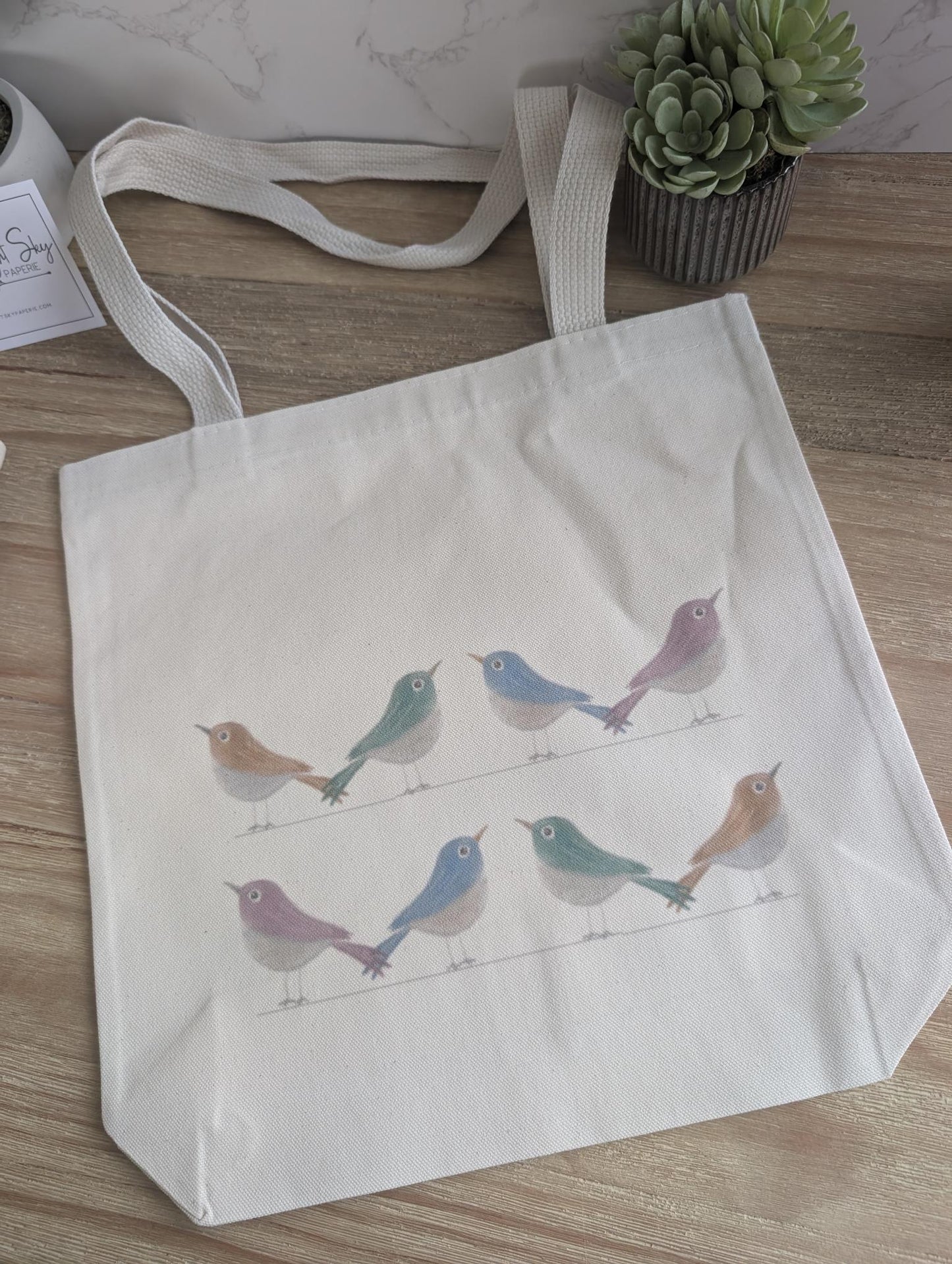 Tote bag with watercolor bird design on a wooden surface
