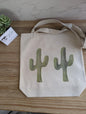 Tote bag with side by side double cactus watercolor design on a wooden surface